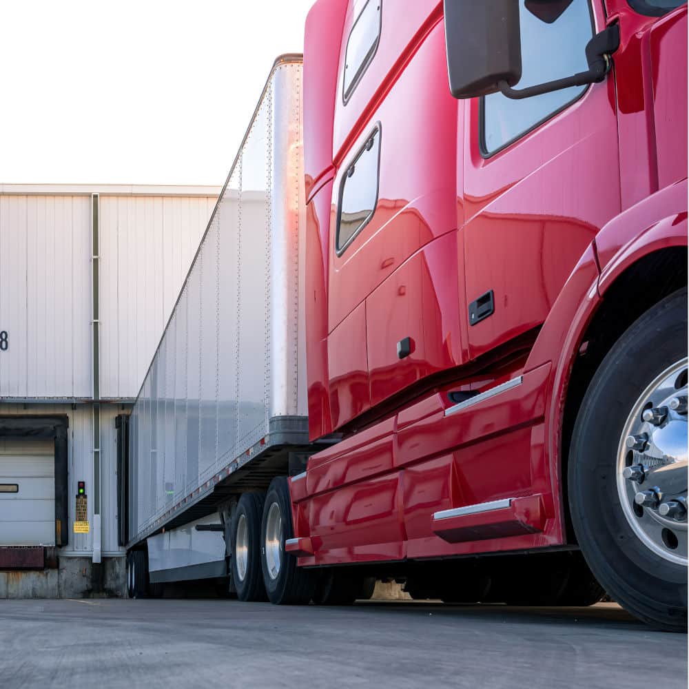 Red modern diesel semi truck parked at a loading dock.